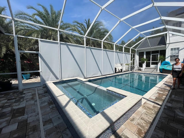 White roller shades around pool and spa with palm trees